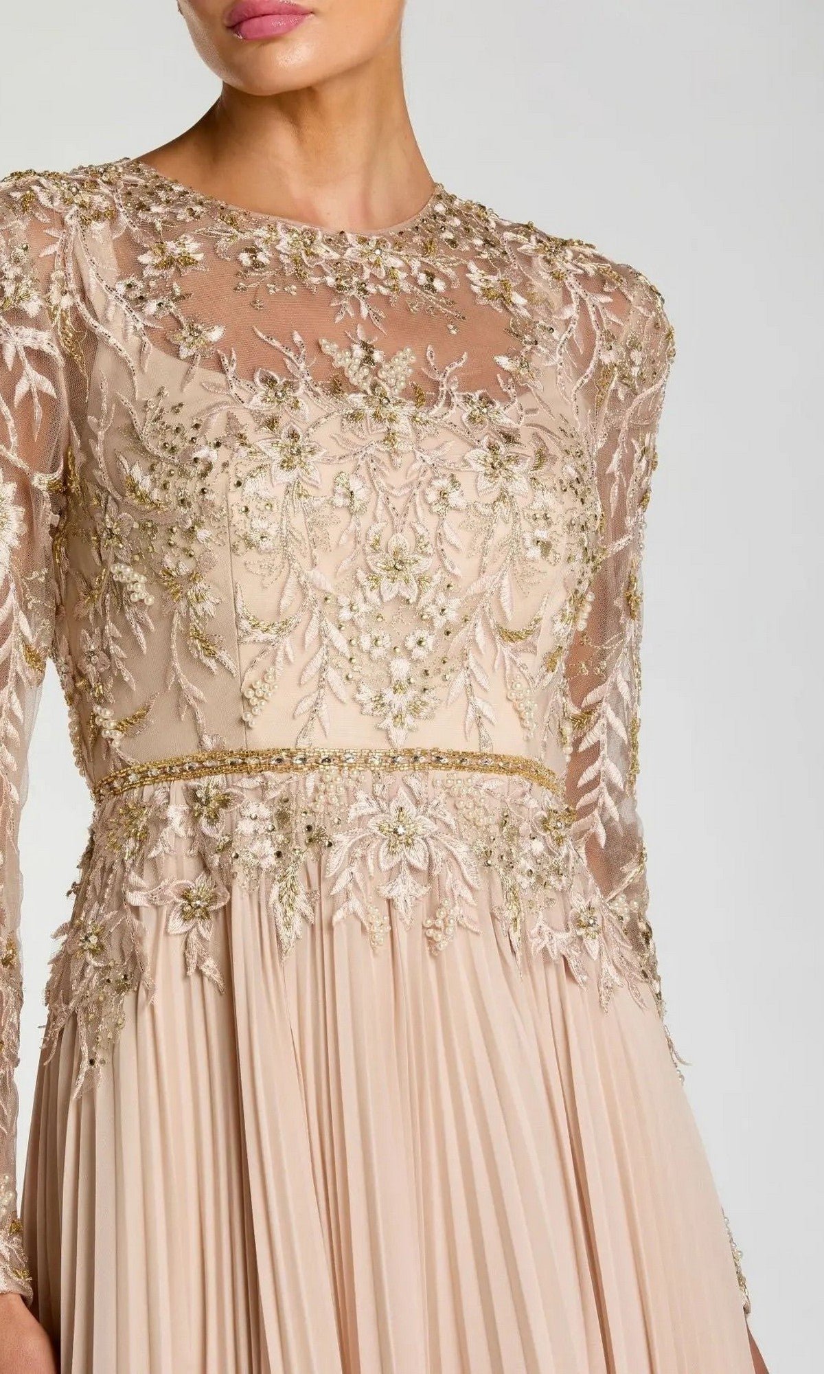 A woman wears the Mac Duggal 11986 long formal dress, featuring beige fabric, gold embroidery, and sheer detailing on the bodice and sleeves.